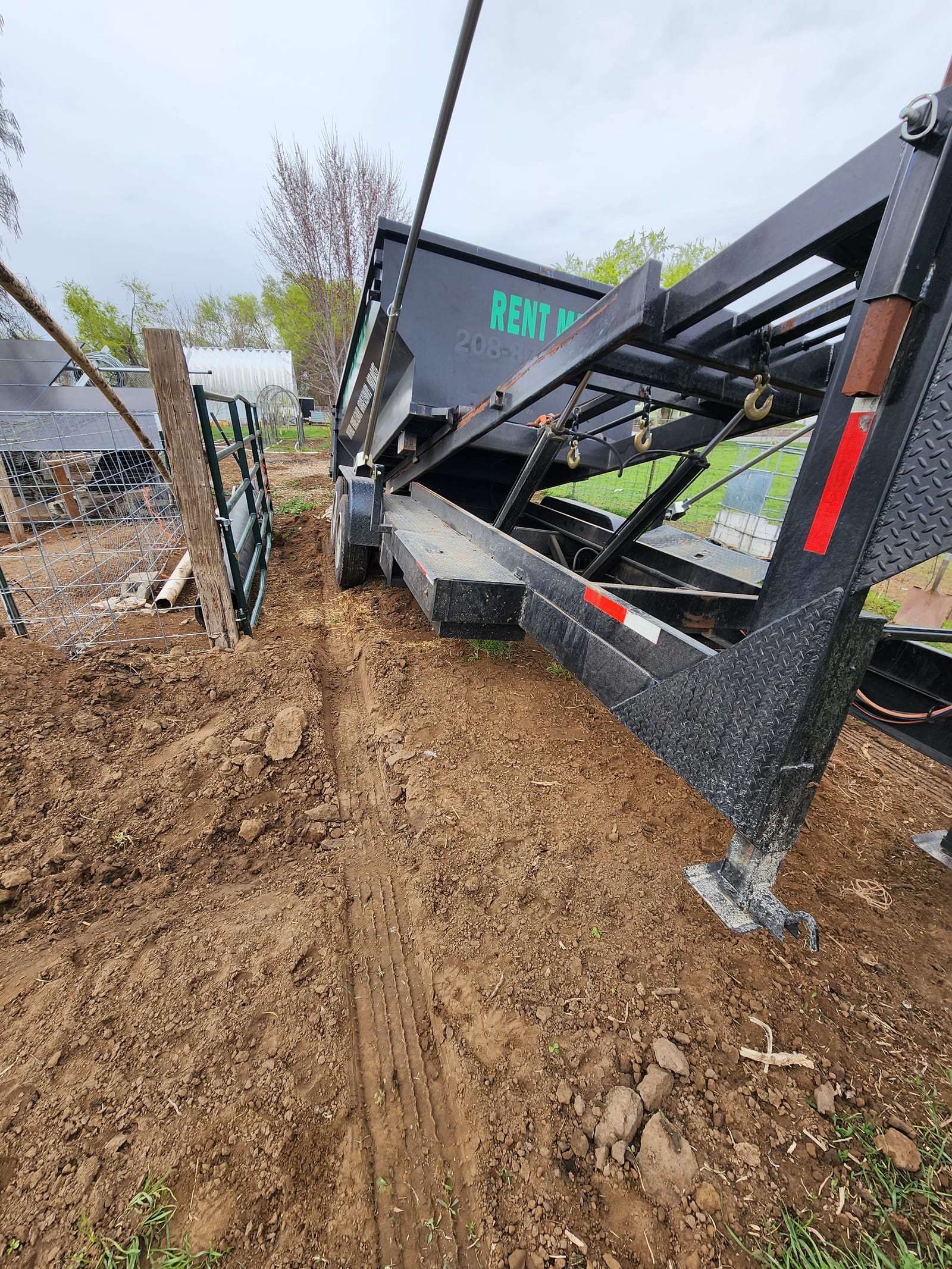 Gooseneck roll-off trailer tipping a dumpster into place at a rural Fruitland jobsite